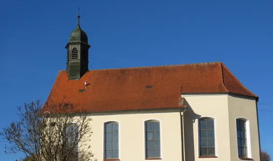 Außenansicht der weißen Kirche mit rotem Dach und Turm bei Sonnenschein.