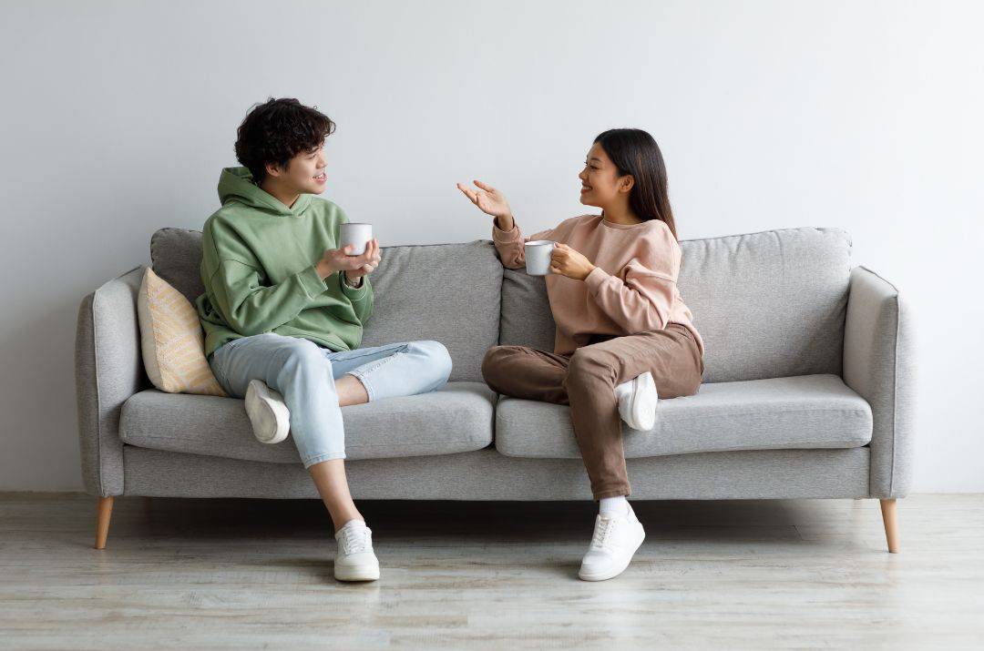 Ein Paar sitzt auf einem grauen Sofa und unterhält sich.