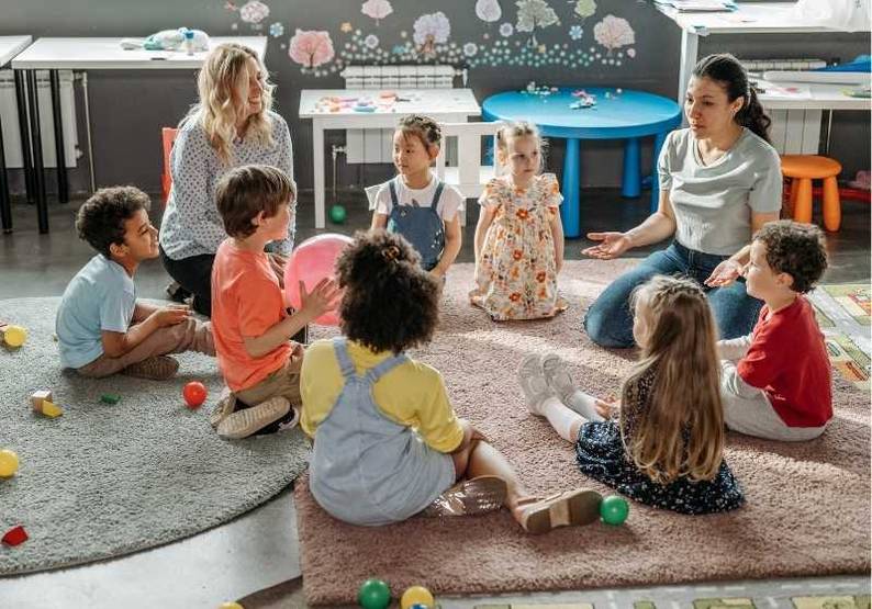 Kinder und Erzieherinnen sitzen in einem Kreis auf dem Boden.